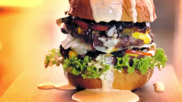 Hamburger, burger. De aproape. un burger suculent, gustos, proaspăt preparat, gras cu cartofi prăjiți și sos, pe o tavă de lemn. fast food, junk food . — Videoclip de stoc