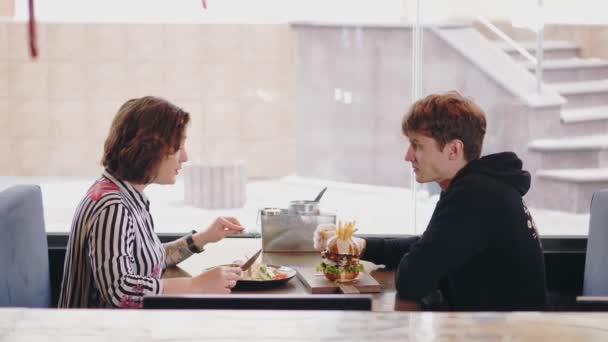 Romantic dinner in cozy cafe. Happy couple of young people have lunch in a cozy, bright restaurant or cafe. young man and woman are smiling, having fun talking. — Stock Video