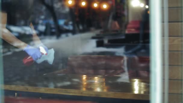 Coronavirus e ristoranti. primo piano. cameriere, in maschera protettiva e guanti, pulizia, pulizia tavolo ristorante utilizzando uno spray antisettico e un tovagliolo di pulizia. vista dalla finestra. pandemia — Video Stock