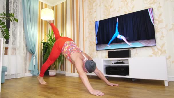 Funny freak. Fat man in multicolored T-shirt and red tight-fitting leggings, is engaged in fitness, fooling around at home. cheerful guy entertains himself, doing aerobic exercises to lose weight, on — Stock Video