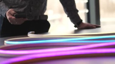 Lider şerit. Yakın plan. Neon bant, lamba. Akıllı telefondaki bir uygulama ile aydınlatma cihazını kontrol etmek. RGBW öncülüğündeki şeridin dinamik, renk değiştirme modu. Yeni ışıklandırma teknolojisi, enerji tasarrufu. Işık dükkânı.