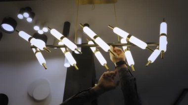 Dükkanda avizeler. Depoda şık lambalarla bir adam moda avizesi gösteriyor. İç tasarım için geniş bir aydınlatma yelpazesi.