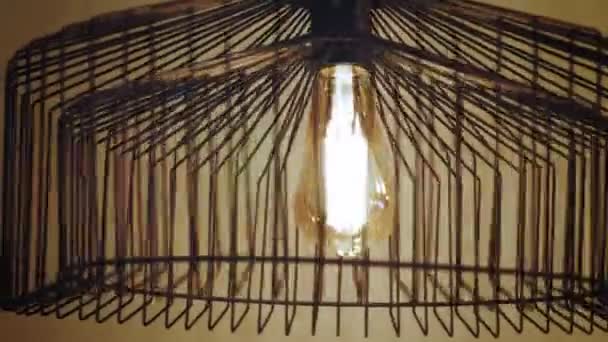 Lampadario di moda. lampada ad incandescenza. primo piano. corpo in metallo del lampadario gira, lasciando belle ombre intorno, sulla parete. lampadina con motivo a spirale, brilla con luce gialla calda. — Video Stock