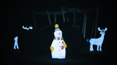 Çelenk heykelleri. Noel Kardan Adam. Geceleyin kardan adam ve ren geyiği heykelleri parkı süsler. Noel çelengi ışıkları.