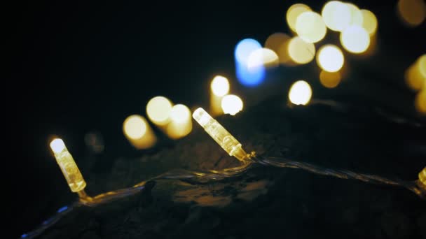 Dekoracyjne lampy LED girlandy. zbliżenie. tło bokeh. złote światła girlanda zdobi pnia drzewa na zewnątrz, w nocy. Świąteczne, świąteczne dekoracje. — Wideo stockowe