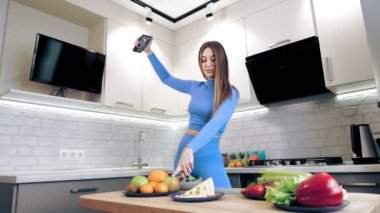 İnternette yemek yapmak. Sağlıklı yemek. Kadın blogcu selfie çekiyor, sosyal medya için akıllı telefondan vejetaryen yemeği videosu çekiyor, ev mutfağında. Mutfak vlogları, sosyal ağlar.