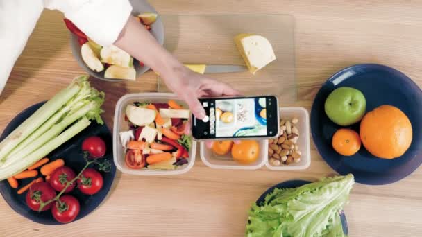Cocinar en línea. comida saludable. Primer plano. Vista superior. Mujer blogger tomando fotos de almuerzo vegetariano en smartphone para redes sociales, en la cocina casera. vlogging culinario, redes sociales. — Vídeos de Stock