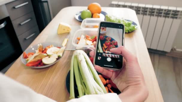 Cocinar en línea. comida saludable. Primer plano. Vista superior. Mujer blogger tomando fotos de almuerzo vegetariano en smartphone para redes sociales, en la cocina casera. vlogging culinario, redes sociales. — Vídeos de Stock