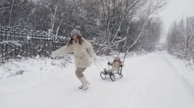 Aile kışın kızakla kayıyor. Açık hava kış aktivitesi. Mutlu, gülen, şakacı çocuklar kar yağarken, ormanda, karlı yolda kızakla kaymaktan zevk alıyorlar. Çocuklar karlı kış gününde eğleniyorlar. yavaş