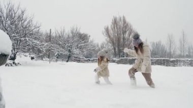 Kış aile aktiviteleri açık havada. Yan görünüş. Küçük mutlu kızlar, çocuklar kar yağarken şehir parkında yavaş yavaş kar altında yürüyorlar. Aile eğleniyor, Karlı 'da birlikte vakit geçiriyorlar.