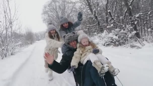 Sanki rodzinne w zimie. zimowa aktywność na świeżym powietrzu. Szczęśliwa, śmiejąca się, zabawna 4-osobowa rodzina cieszy się ze zjeżdżania swoich dzieci na śnieżnej drodze, w lesie, podczas opadów śniegu. rodzina dobrze się bawi — Wideo stockowe