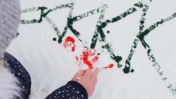 Zimní zábava. dítě kreslí barvy ve sněhu. detailní záběr. kreslení na sněhu. bavte se na zasněžené zimní den, venku. — Stock video