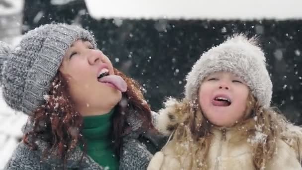 Zimowa rodzinna zabawa. złapać płatki śniegu z języka. Szczęśliwa rodzina, matka i córka łapią płatki śniegu swoimi językami, cieszą się śniegiem i opadami śniegu, dobrze się bawią, spędzają razem czas — Wideo stockowe