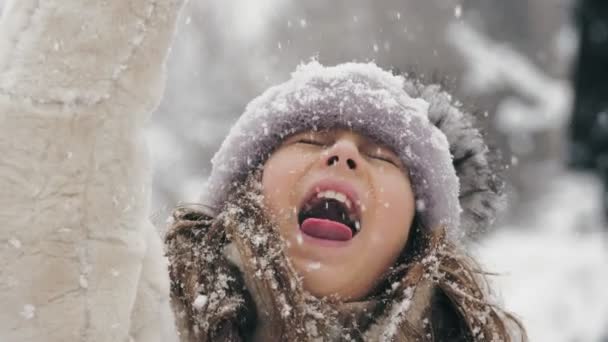 Χειμωνιάτικη οικογενειακή διασκέδαση. πιάσει νιφάδες χιονιού με τη γλώσσα. Ευτυχισμένο χαριτωμένο, όμορφο κοριτσάκι πιάνει νιφάδες χιονιού με τη γλώσσα της, απολαμβάνοντας το χιόνι και τις χιονοπτώσεις, διασκεδάζοντας την χιονισμένη χειμωνιάτικη μέρα. αργή κίνηση. — Αρχείο Βίντεο