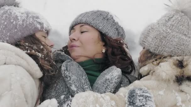 Vinterfamiljens nöje. Lycklig mor med små döttrar ligger, rullande i snö, njuta av snö och snö, kyssas, ha kul utomhus, tillbringa tid tillsammans på snöiga vinterdag i parken eller — Stockvideo