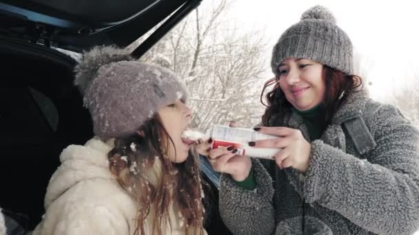 Zimní čajový piknik, venku. Šťastné dítě jí šlehačku ze spreje, trubice. šťastný čas na zasněžené zimní den, během sněžení. — Stock video