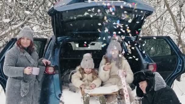 Vinterte picknick. Lycklig familj har gott mellanmål, en tebjudning med grädde, utomhus. De sitter på bagageluckan, i snöig skog, under snöfall. vinterfamiljens nöje. Glad tid på snöig vinter — Stockvideo