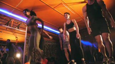 Crossfit jimnastik. Spor salonunda grup fitness. Spor, fitness takım çalışması. Küçük formda bir grup, erkek ve bayan sporculardan oluşan yaya geçidi takımı spor salonunda, loş ışıkta, renkli ışıklarla birlikte çalışıyor.