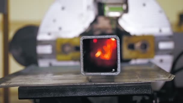 金属パイプ用レーザー切断機。接近中だ。CNCファイバーレーザーを備えた現代的なマシンは正方形の金属パイプを切断しています。明るい燃焼火花は、切断プロセス中にレーザービームから飛ぶ — ストック動画