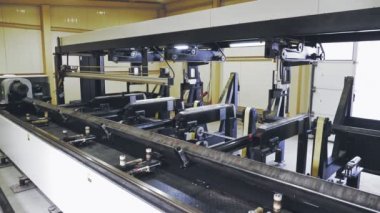 Metal borular için lazer kesme makinesi. Kare metal boru hareket ediyor ve dönüyor, atölyedeki akıllı CNC endüstriyel makinesinin klipsleri ve pnömatik kıskaçlar tarafından tutuluyor. Modern, akıllı, CNC çalışma süreci