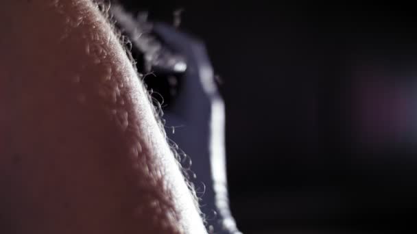 Hårborttagning. Hårdhet. närbild. Hand i handske klipper manliga kroppshår med en elektrisk hårklippare, maskin. förfarande för manliga kroppen hårklippning i skymning, i strålar av ljus. Kroppsvård. — Stockvideo