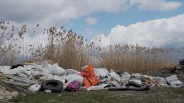 Nehrin yanındaki çöplükte. Ekolojik bir sorun. Nehrin kıyısındaki yasadışı inşaat atığı. Çöp yığını, çöp, dışarı atılmış. Fıçı. Çevre kirliliği.