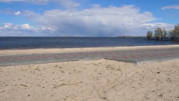 Wiosenny krajobraz piaszczystej plaży nad rzeką lub morzem, błękitne niebo z chmurami, w słoneczny dzień. w ruchu. chodnik wzdłuż plaży. krajobraz morski w słoneczny wiosenny dzień. — Wideo stockowe