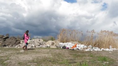 Dışarıdaki çöpler. Nehrin yanındaki çöplükte. Kadın, gönüllü, plastik çöp torbasıyla nehrin kıyısındaki yasadışı inşaat atığının yanından geçiyor çöp yığınları, çöp yığınları, açık havaya atılıyor.