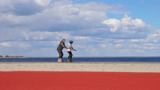 Patinação em patins ao ar livre. patinagem ao ar livre. adolescente está aprendendo patinação rolo com a ajuda de seu pai. pai está ensinando filha patinando ao ar livre, em um caminho ao lado da praia — Vídeo de Stock