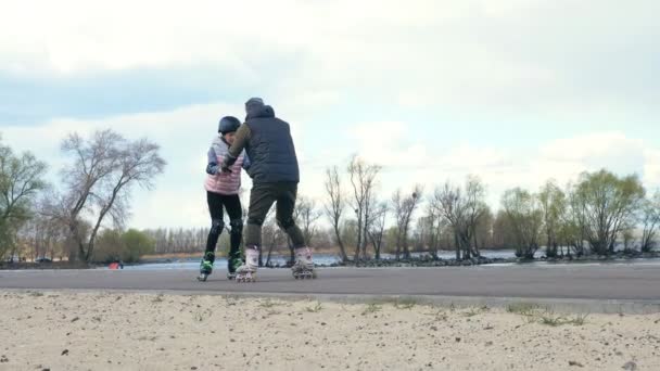 Patinação em patins ao ar livre. patinagem ao ar livre. adolescente está aprendendo patinação rolo com a ajuda de seu pai. pai está ensinando filha patinando ao ar livre, em um caminho ao lado da praia — Vídeo de Stock