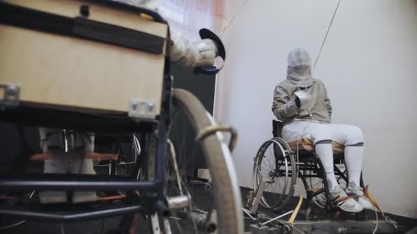 Niepełnosprawny sportowiec. szermierka. biały szermierka umundurowani szermierki, na wózkach inwalidzkich, z ogrodzenia kaski bezpieczeństwa na ich twarzach, trzymają gwałcicieli i sparing na treningu. — Wideo stockowe