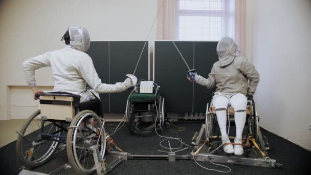 Atleta com deficiência. Esgrima. esgrima branca esgrimistas uniformizados, em cadeiras de rodas, com capacetes de segurança esgrima em seus rostos, estão segurando rapiers e sparring no treino. — Vídeo de Stock