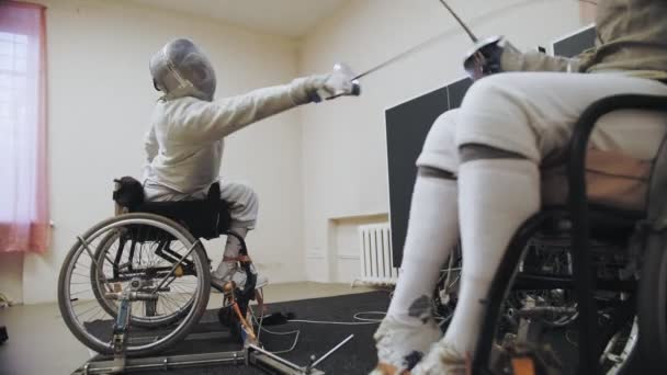 Athlète handicapé. Clôture. escrime blanche escrimeurs en uniforme, en fauteuil roulant, avec des casques de sécurité clôture sur leurs visages, tiennent rapières et sparring à l'entraînement. — Video