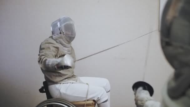장애인 운동 선수. 펜싱. 흰 펜싱을 하고 있는 제복을 입은 사람들 이 휠체어를 타고 얼굴에 울타리를 치고 레이저와 스파링을 하고 있습니다. — 비디오