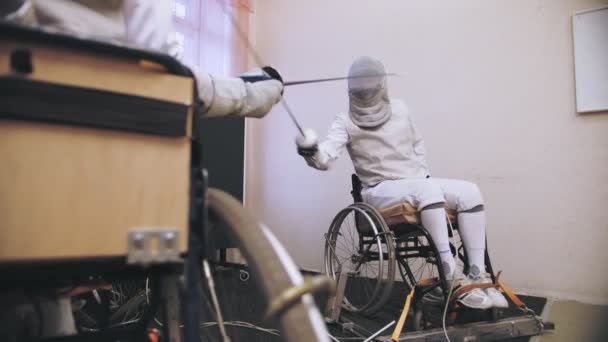 Disabled athlete. fencing. sparring in fencing duel of two wheelchair fencing athletes with reduced physical abilities. They practice fight duel technique during workout. — Stock Video