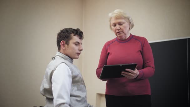 Gehandicapte atleet. Omheining. workout van rolstoelschermen atleten met beperkte lichamelijke vermogens. Vrouwelijke trainer toont vechten duel techniek op digitale tablet. — Stockvideo