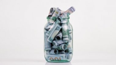Para için. Dolar banknotları. Yakın plan. Döndürme. Cam bir kavanozda yuvarlanmış yüz dolarlık banknotlar döner döner döner döner, beyaz arka planda.