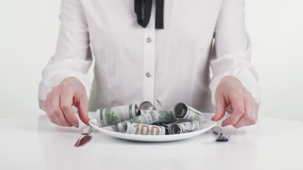 Mujer de negocios y dinero, efectivo. Primer plano. una mujer de negocios, en blusa blanca de negocios, mezcla billetes de cien dólares enrollados en un plato con cubiertos, cuchillo y tenedor en sus manos. Parece que se va. — Vídeos de Stock