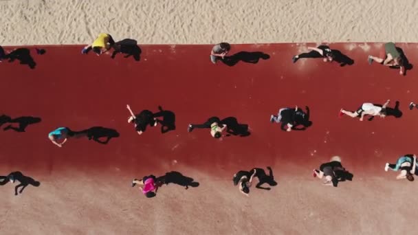 Entrenamiento de fitness en grupo al aire libre. fitness al aire libre. Gran grupo de personas, con ropa deportiva, está haciendo ejercicio, yendo a hacer deporte juntos, en la playa, junto al río o al mar, al aire libre. aero, arriba — Vídeos de Stock