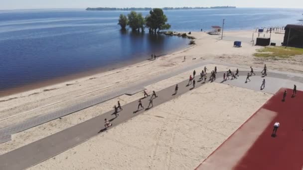 Grupowy trening fitness na zewnątrz. fitness na świeżym powietrzu. widok z powietrza. Duża grupa ludzi, ubrana w strój aktywny, ćwiczy, uprawia razem sport, na plaży, nad rzeką lub morzem, na świeżym powietrzu — Wideo stockowe