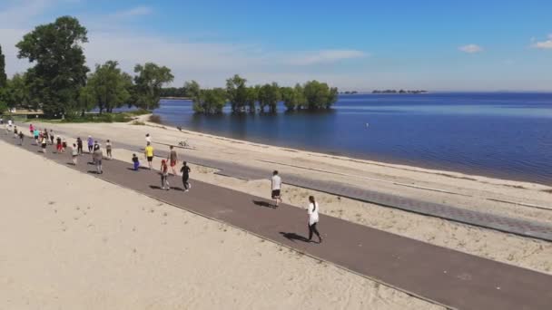 Entrenamiento de fitness en grupo al aire libre. fitness al aire libre. Gran grupo de personas, con ropa deportiva, está haciendo ejercicio, yendo a hacer deporte juntos, en la playa, junto al río o al mar, al aire libre. saludable — Vídeo de stock