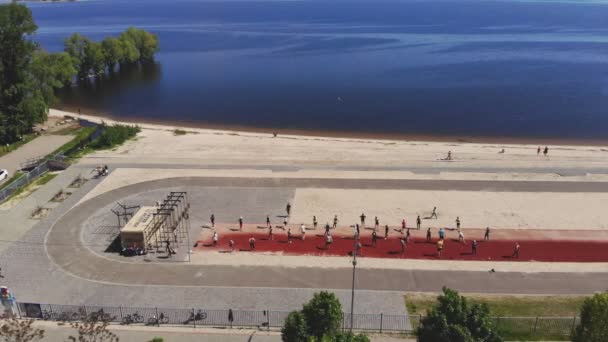 Entrenamiento de fitness en grupo al aire libre. fitness al aire libre. Vista aérea. Gran grupo de personas, con ropa deportiva, está haciendo ejercicio juntos, en la playa, junto al mar, al aire libre. concepto de estilo de vida saludable. deporte — Vídeos de Stock