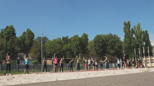 Gruppen-Fitnesstraining im Freien. Fitness im Freien. Eine große Gruppe von Menschen in Aktivkleidung trainiert gemeinsam, auf dem Sportplatz, am Strand, im Freien. gesunder Lebensstil. Sport im Freien — Stockvideo