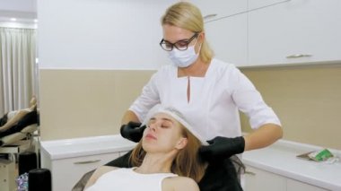 Kadınlar için kozmetik prosedürler. Kozmetoloji. Kozmetik ameliyat için hazırlık. Güzellik uzmanı, kozmetik ameliyatına başlamadan önce bir kadının kafasına tek kullanımlık bir şapka takar ve saçlarını saklar. Güzellikte