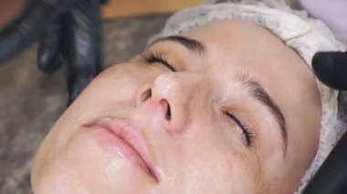 beauty therapy. sun protection. close-up, cosmetician in black medical gloves, applies sunscreen or evenly cosmetic cream to female face with massage movements. Facial rejuvenation. skincare