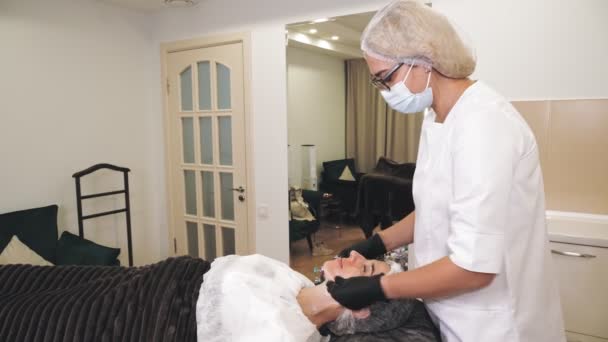 Beauty therapy. facial massage. Cosmetology skin care. beautician, in medical mask and gloves, performs facial skincare massage for woman, at beauty clinic. anti-aging procedure. Facial rejuvenation. — Stockvideo