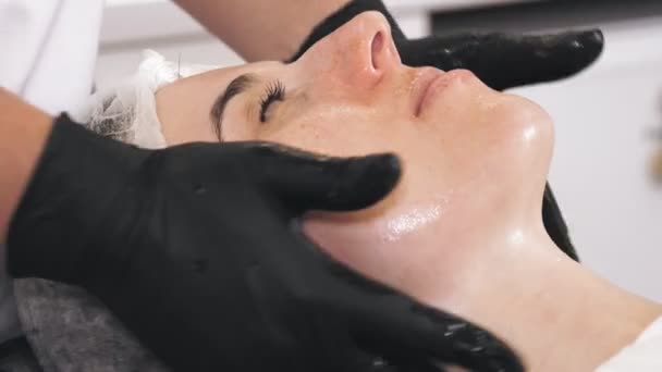 Terapia de belleza. masaje facial. Cosmetología cuidado de la piel. Primer plano. mujer está recibiendo masaje facial cuidado de la piel, tonied la piel facial y los músculos, haciendo drenaje linfático, en la clínica de belleza. antienvejecimiento — Vídeo de stock