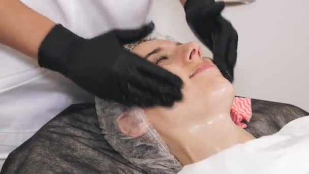 Beauty therapy. Cosmetology skin care. beautician in black medical gloves performs cosmetic skincare procedure, applies cleansing foam or emulsion to female face. close-up. anti aging procedure — Stockvideo
