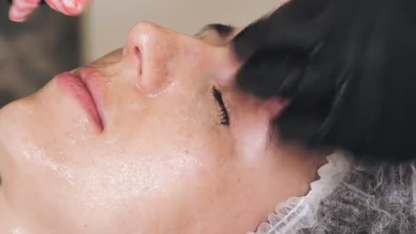 Terapia di bellezza. Cosmetologia cura della pelle. primo piano. il cosmetologo, in guanti medici neri, toglie resti di prodotto di faccia cosmetico, da faccia femminile con salviettine umide speciali. procedura anti invecchiamento. Viso — Video Stock