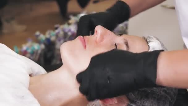 Beauty therapy. Cosmetology skin care. close-up. cosmetologist, in black medical gloves, removes remains of cosmetic face product, from female face with special wet wipes. anti aging procedure. Facial — Stockvideo
